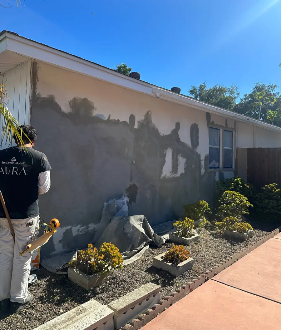 Before: the same side wall mid-repair, with patched gray stucco while a Lotus crew member works